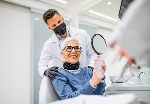 Woman in dental chair admiring reflection with dentist touching her shoulders
