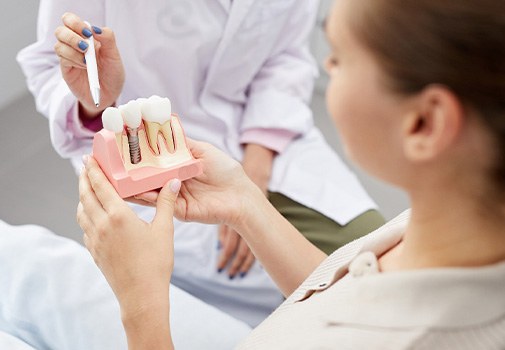 Dentist pointing to model implant held by patient
