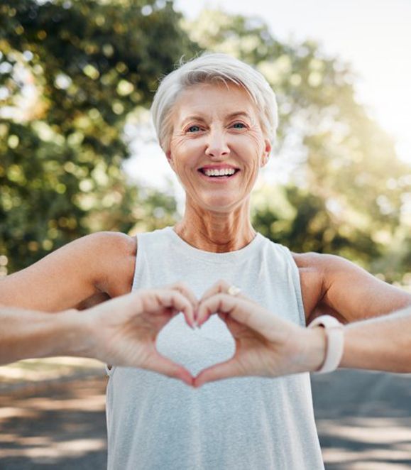 Lady smiles while making shape of a heart with her hands outdoors